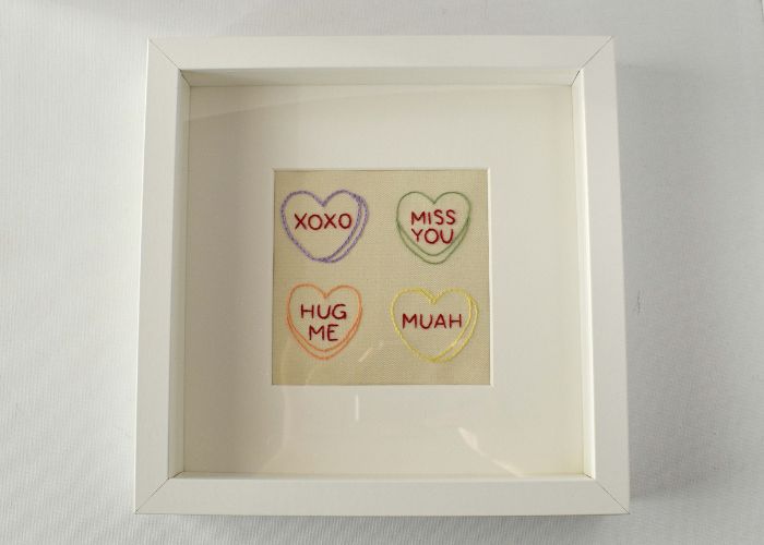 Ricamo di cuori di caramelle incorniciato in una cornice shadowbox bianca